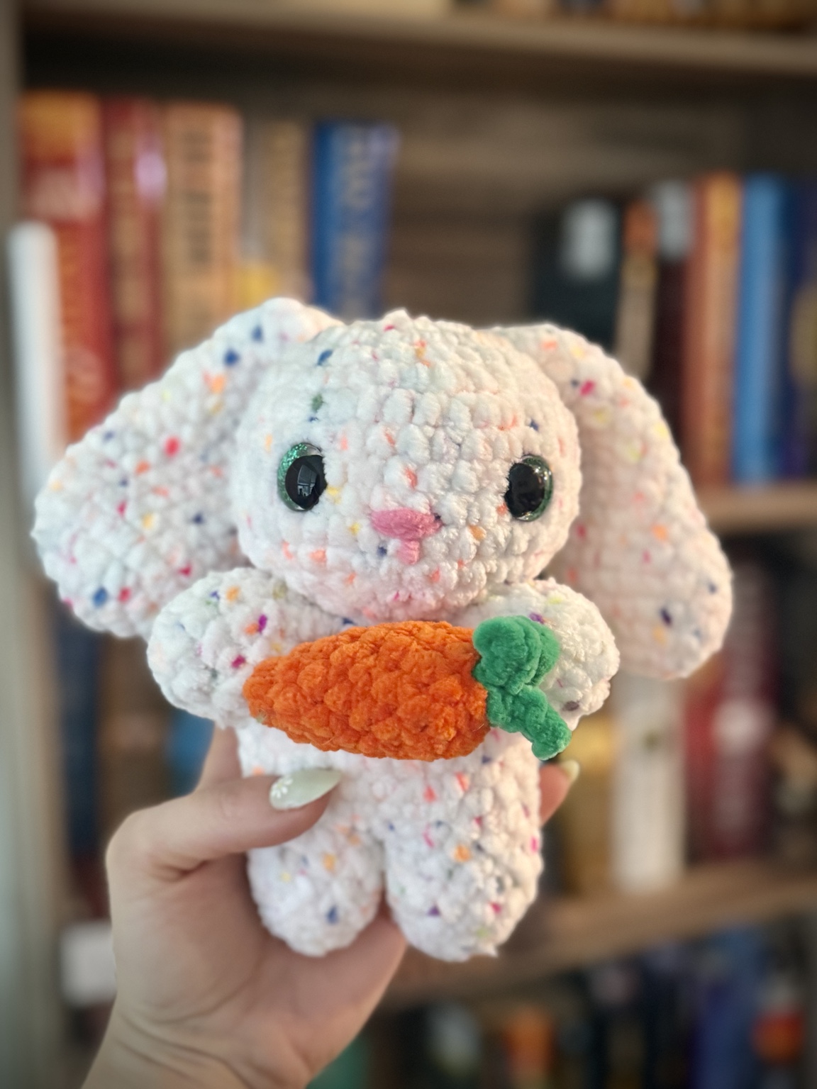White pastel-speckled crochet bunny holding an orange carrot.