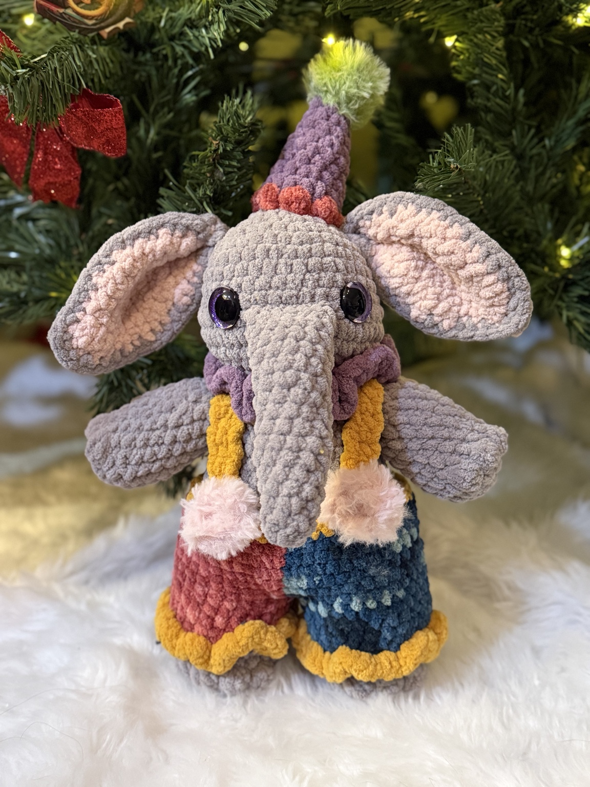 Gray crochet elephant dressed as a clown with a colorful pointed hat and patchwork outfit.
