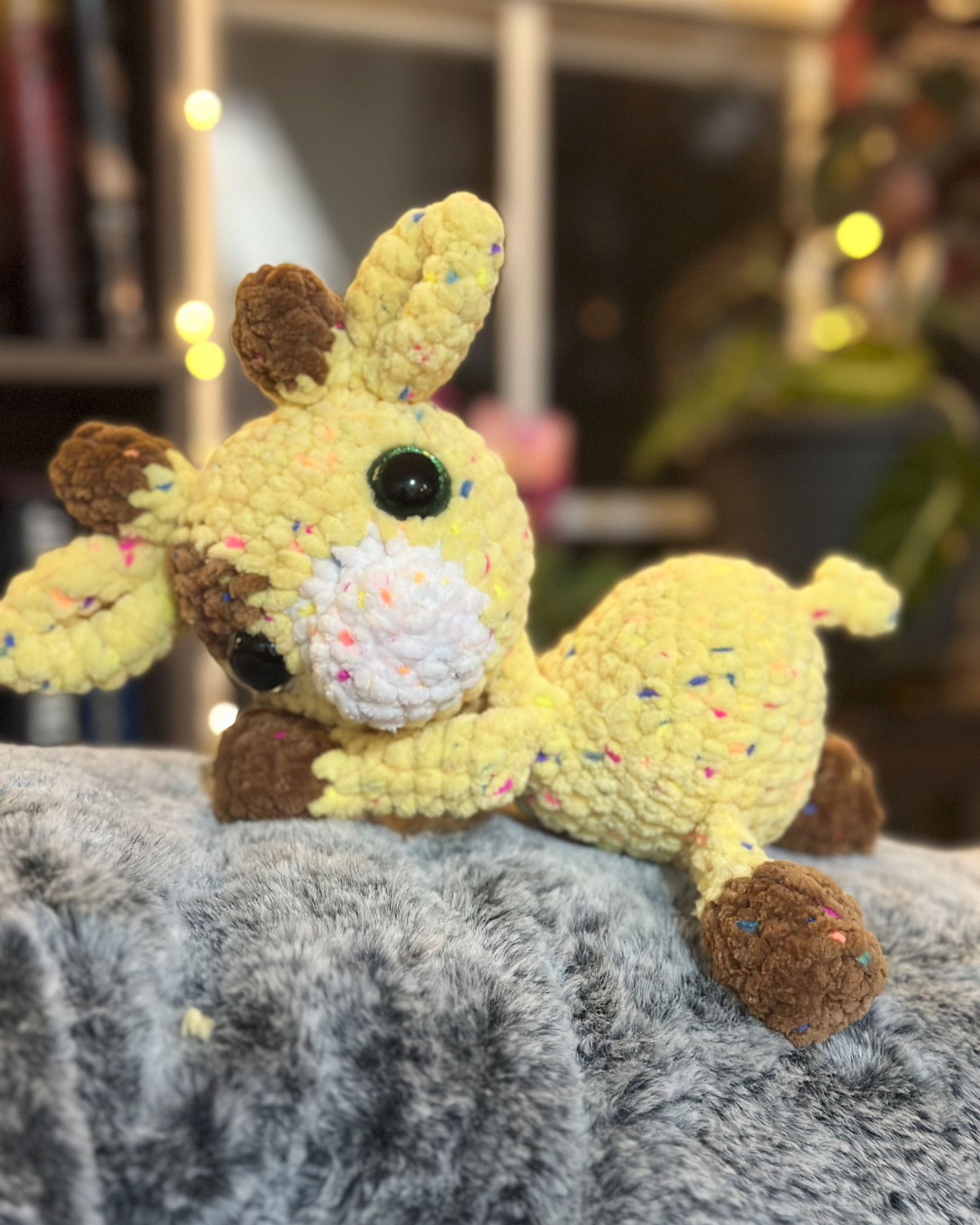 Yellow crochet giraffe with brown spots attached to a soft yellow blanket.