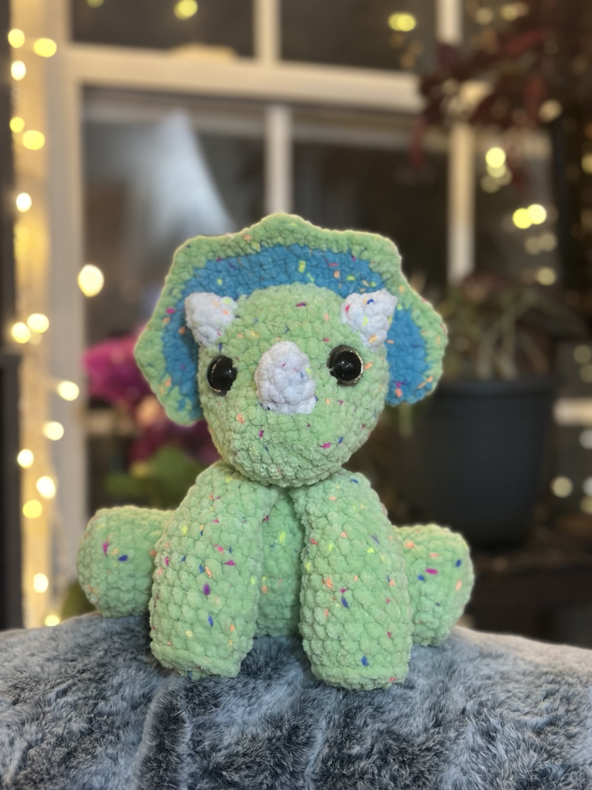 Green crochet triceratops with blue frill details and cream horns.