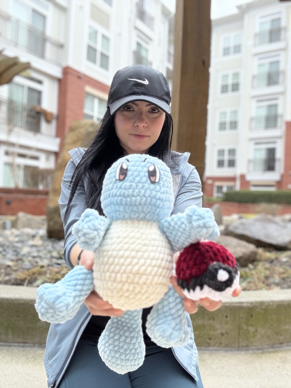 Ina holding her handmade blue crochet character and a red and white crochet ball outdoors.