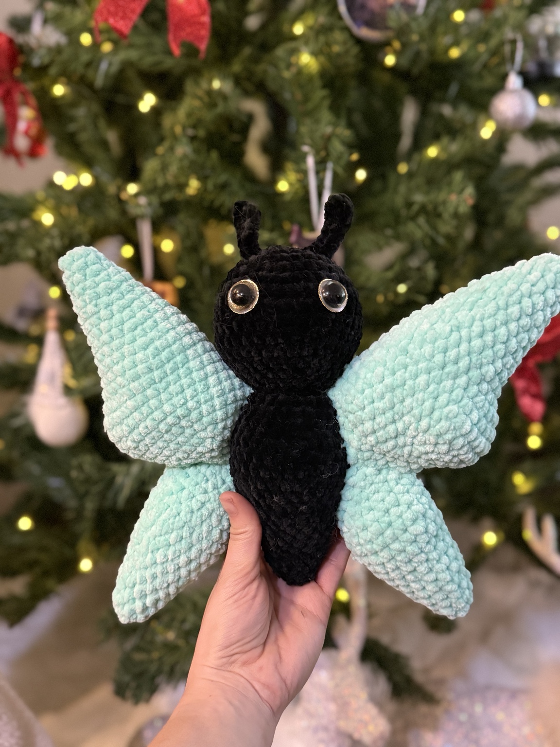 Black crochet butterfly with large mint green wings, held in front of a Christmas tree.