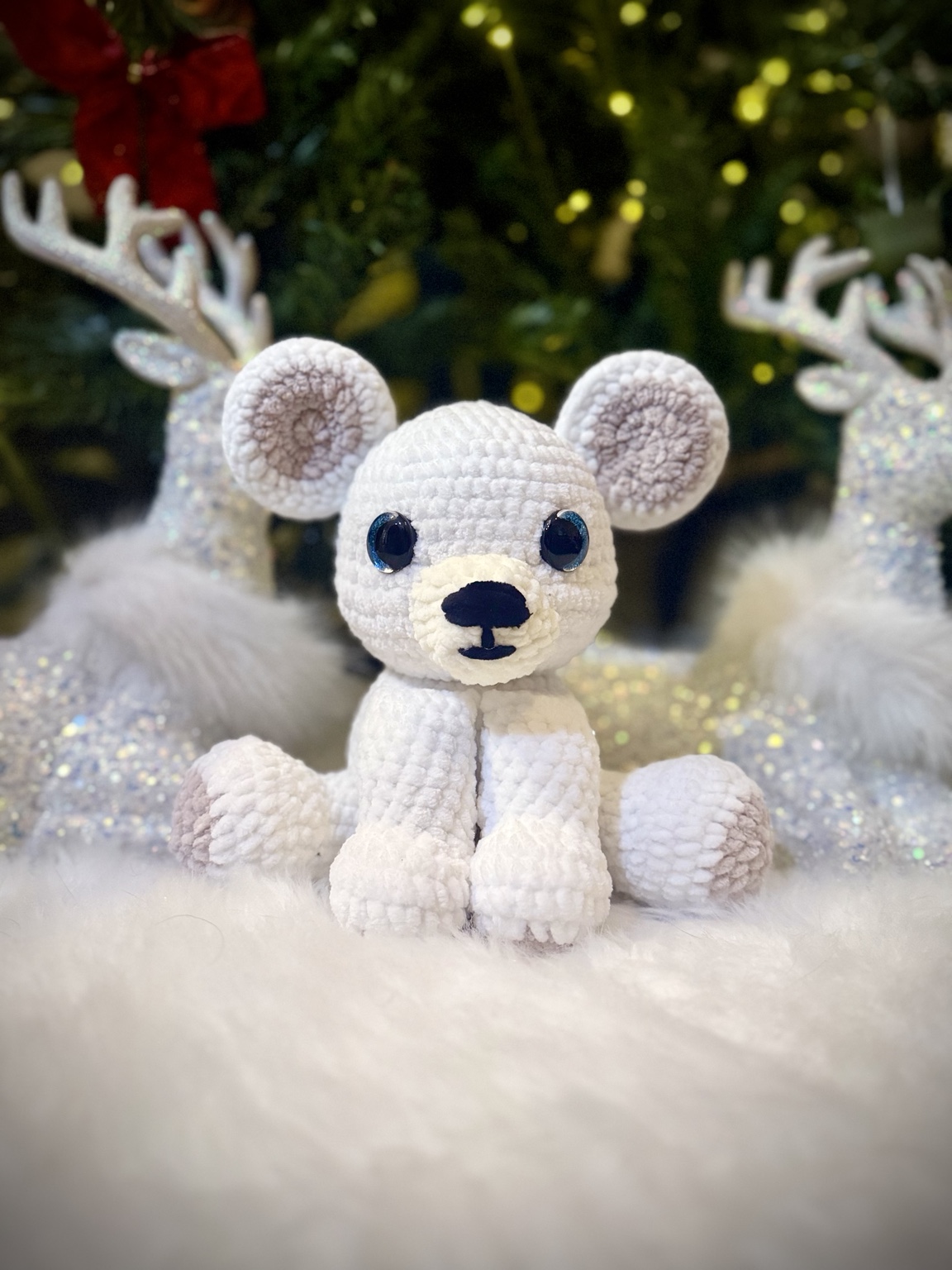 White crochet polar bear with pale gray ears and paws beside decorative reindeer.