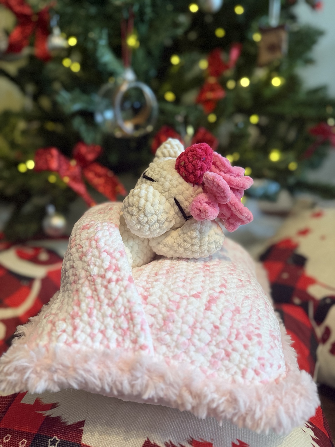 Cream crochet unicorn with pink details attached to a soft pastel blanket.