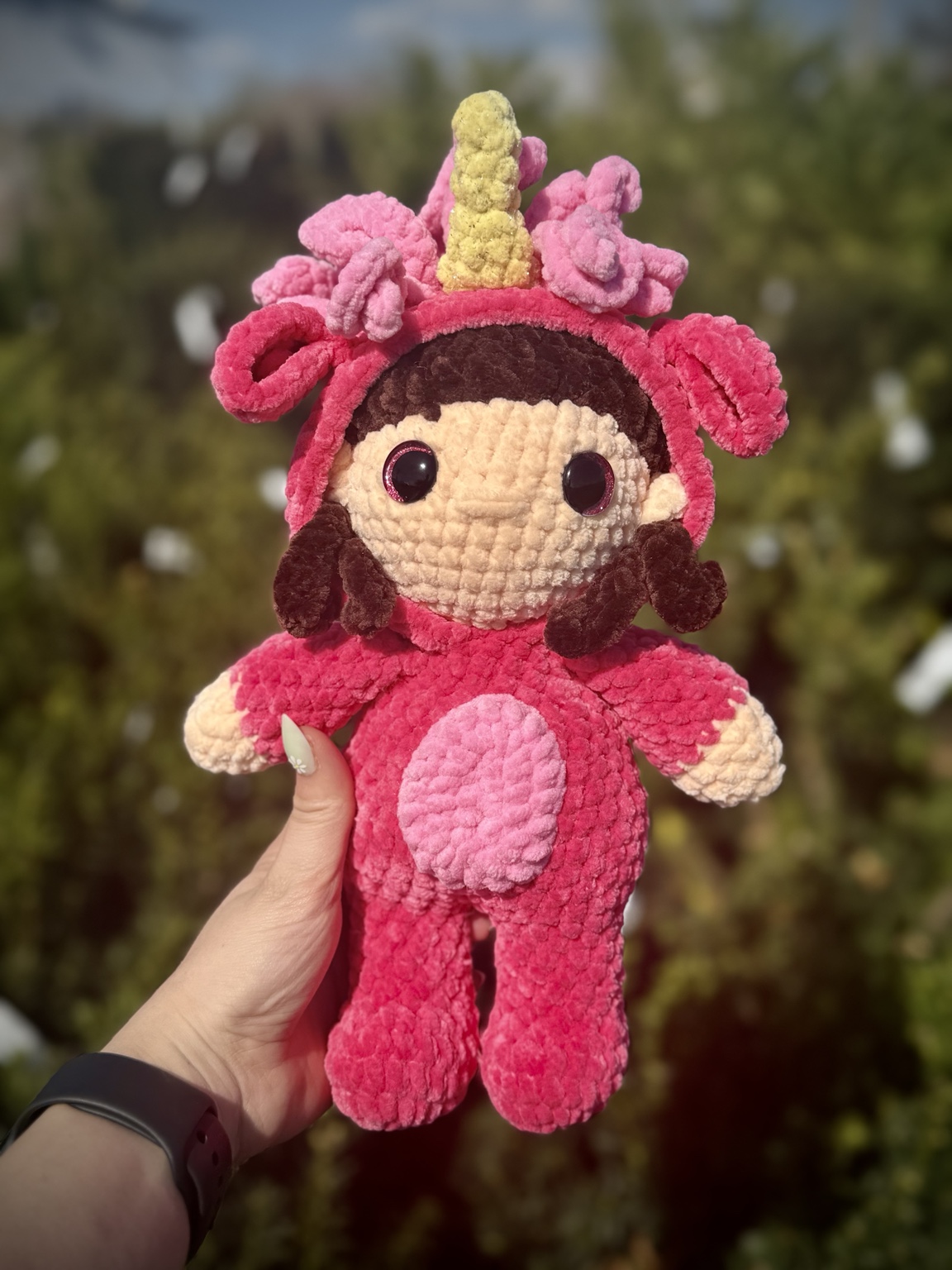 Crochet girl doll wearing bright pink unicorn pajamas with a yellow horn.